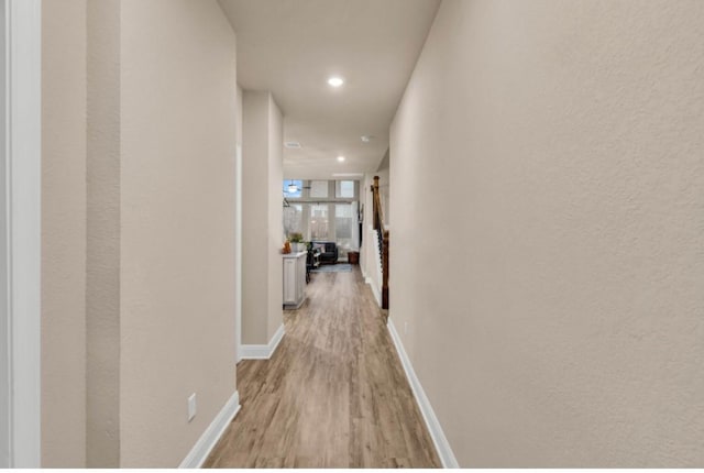 hallway with light wood-type flooring, baseboards, and recessed lighting