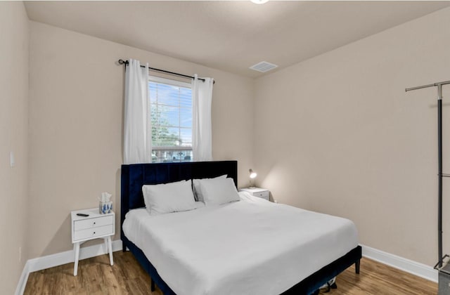 bedroom with baseboards, visible vents, and wood finished floors