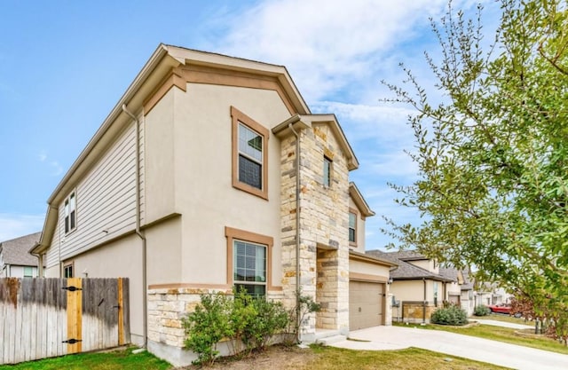 view of side of home featuring stone siding, fence, concrete driveway, and stucco siding