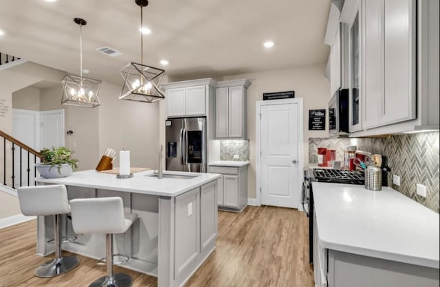 kitchen featuring stainless steel appliances, light countertops, visible vents, a sink, and light wood-type flooring