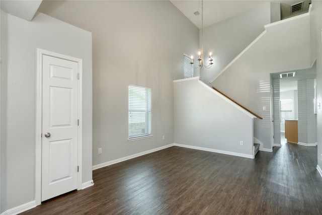 unfurnished living room featuring a high ceiling, an inviting chandelier, and dark hardwood / wood-style flooring