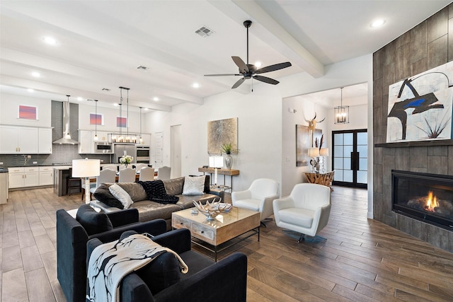 living room featuring hardwood / wood-style flooring, a fireplace, beamed ceiling, and ceiling fan with notable chandelier