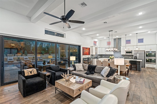 living room with sink, ceiling fan with notable chandelier, and beamed ceiling