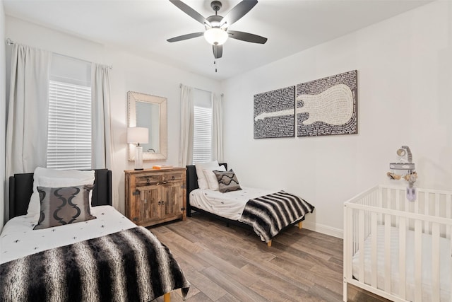 bedroom with multiple windows, hardwood / wood-style floors, a nursery area, and ceiling fan