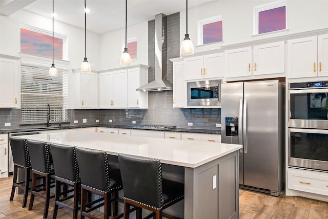 kitchen featuring a center island, white cabinets, pendant lighting, stainless steel appliances, and wall chimney range hood