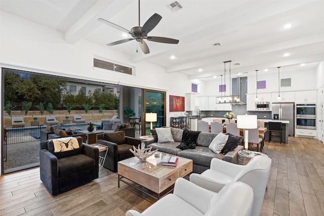 living room featuring ceiling fan, beam ceiling, sink, and a towering ceiling