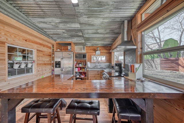 interior space with vaulted ceiling, appliances with stainless steel finishes, wood walls, sink, and wall chimney range hood