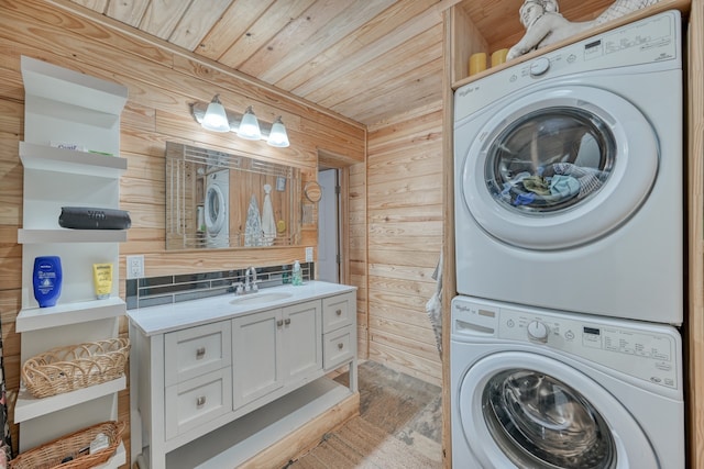 clothes washing area featuring sink, wood ceiling, wooden walls, and stacked washing maching and dryer