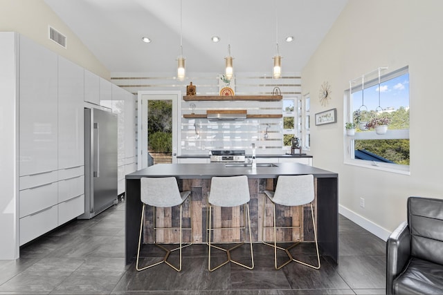 kitchen featuring decorative light fixtures, white cabinetry, lofted ceiling, an island with sink, and stainless steel appliances