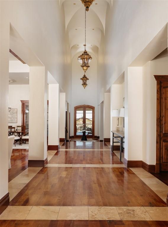 foyer entrance with arched walkways, baseboards, french doors, wood-type flooring, and an inviting chandelier