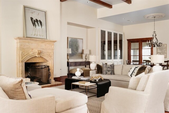 living area featuring wood finished floors, beamed ceiling, an inviting chandelier, and a premium fireplace