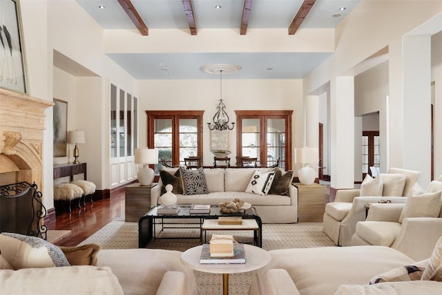 living area featuring a fireplace, a towering ceiling, wood finished floors, a chandelier, and beamed ceiling