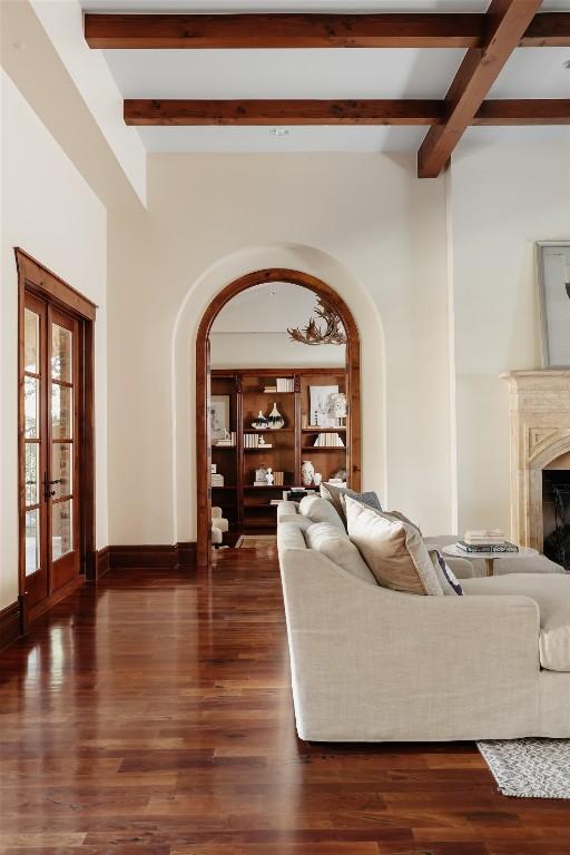 living area with arched walkways, a fireplace, wood finished floors, baseboards, and beamed ceiling