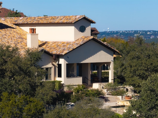 rear view of house featuring a tiled roof, a chimney, and stucco siding