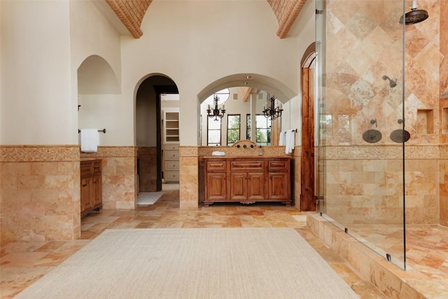 bathroom with a wainscoted wall, tile walls, a towering ceiling, a stall shower, and vanity