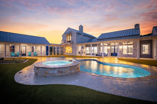 pool at dusk with an in ground hot tub and a patio area