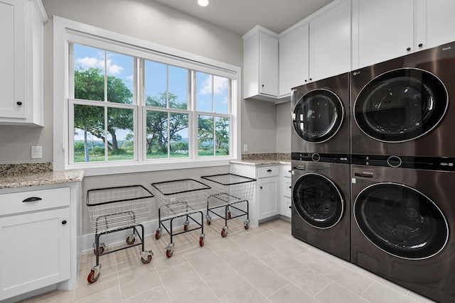 clothes washing area with stacked washer and dryer, light tile patterned floors, and cabinets