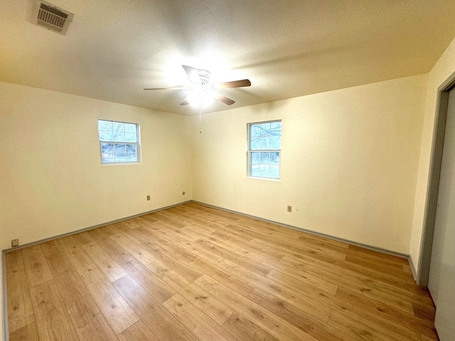 empty room with ceiling fan, a healthy amount of sunlight, light hardwood / wood-style floors, and a textured ceiling