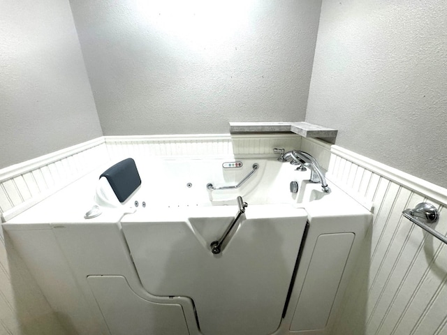 washroom featuring washer / dryer, a textured wall, and wainscoting