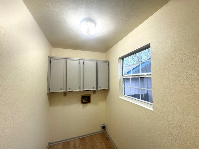 clothes washing area with baseboards, cabinet space, a textured wall, and wood finished floors