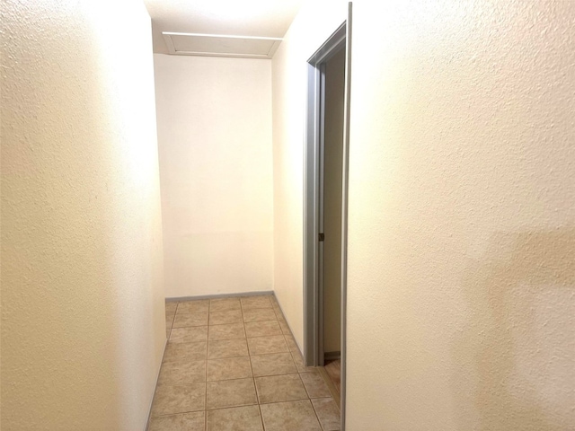 corridor with light tile patterned flooring, a textured wall, and attic access