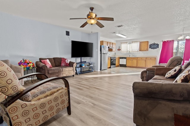 living room featuring ceiling fan, plenty of natural light, light hardwood / wood-style floors, and a textured ceiling