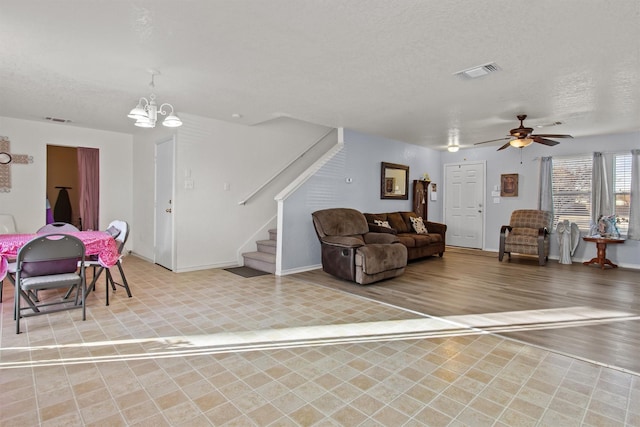 living room with ceiling fan with notable chandelier and a textured ceiling