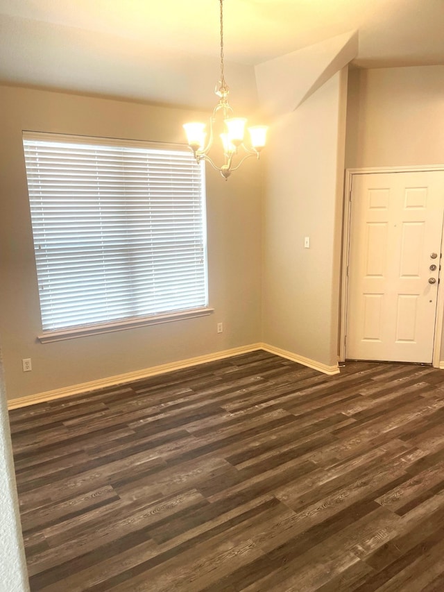 spare room with dark wood-type flooring, plenty of natural light, and a notable chandelier