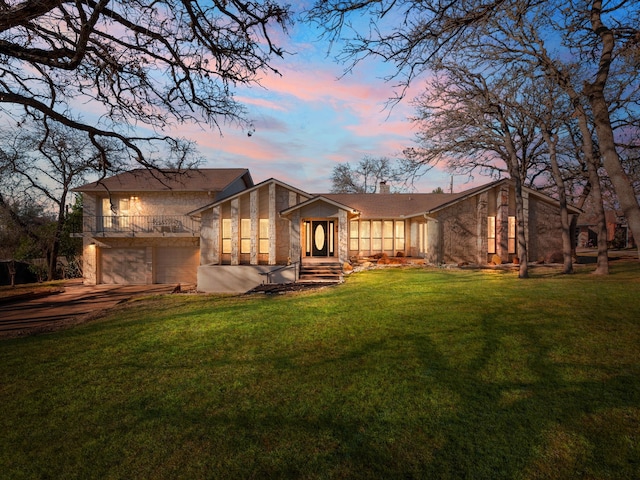 back house at dusk featuring a garage and a lawn