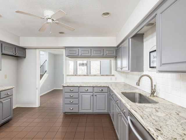 kitchen featuring decorative backsplash, gray cabinetry, a sink, light stone countertops, and dark tile patterned flooring