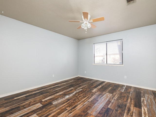 spare room featuring a ceiling fan, visible vents, dark wood finished floors, and baseboards