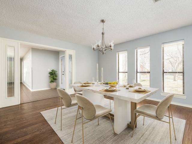 dining area with an inviting chandelier, a textured ceiling, baseboards, and wood finished floors