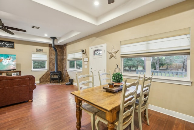 dining room with a tray ceiling, hardwood / wood-style flooring, ceiling fan, and a wood stove