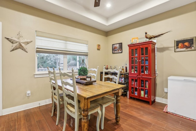 dining space featuring wood-type flooring, ceiling fan, and a tray ceiling