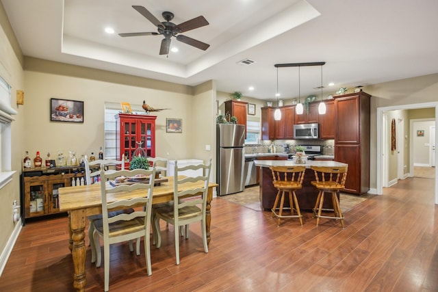 dining room featuring dark wood-type flooring, ceiling fan, and a tray ceiling