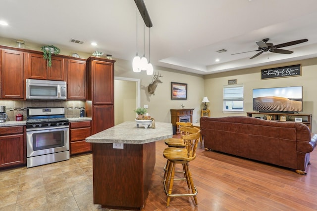 kitchen with a breakfast bar, appliances with stainless steel finishes, decorative backsplash, a kitchen island, and decorative light fixtures