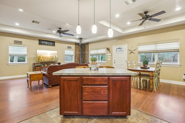 kitchen with hanging light fixtures, a wood stove, a raised ceiling, a kitchen island, and ceiling fan