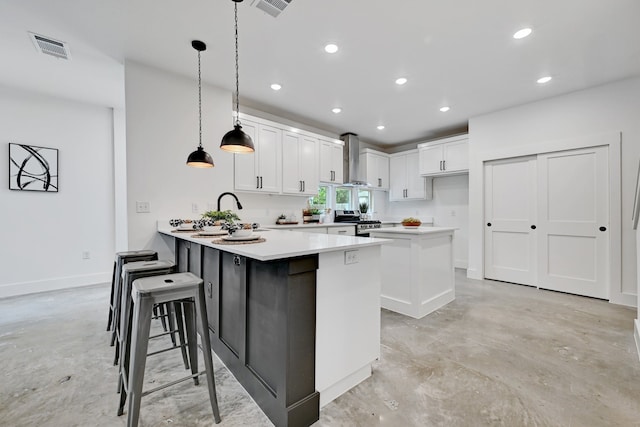 kitchen featuring pendant lighting, wall chimney range hood, stainless steel stove, white cabinets, and kitchen peninsula