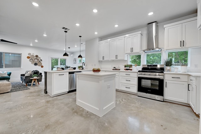 kitchen with appliances with stainless steel finishes, hanging light fixtures, white cabinets, kitchen peninsula, and wall chimney exhaust hood