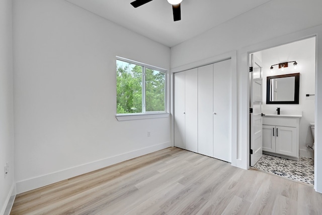 unfurnished bedroom with ensuite bath, a closet, ceiling fan, and light wood-type flooring