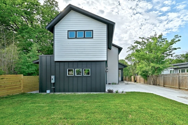 rear view of house featuring concrete driveway, a fenced backyard, a yard, a patio area, and board and batten siding