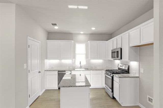 kitchen with a kitchen island, appliances with stainless steel finishes, sink, white cabinets, and light stone countertops