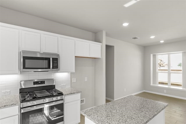 kitchen featuring light hardwood / wood-style flooring, white cabinetry, backsplash, stainless steel appliances, and a center island