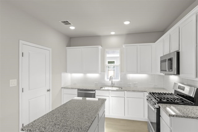 kitchen featuring stainless steel appliances, sink, white cabinets, and light stone counters