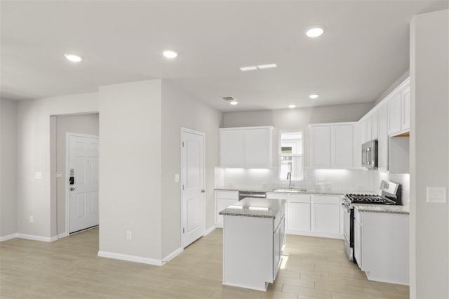 kitchen with sink, white cabinetry, a kitchen island, stainless steel appliances, and light stone countertops