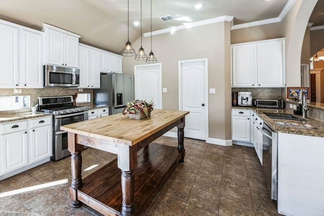 kitchen with sink, white cabinetry, hanging light fixtures, dark stone counters, and stainless steel appliances