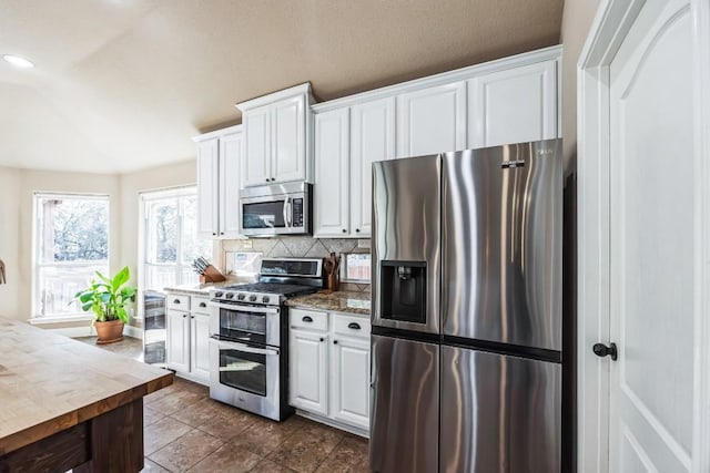 615 Mountain Crest Dr, Wimberley, TX 78676 - kitchen with stainless steel appliances, white cabinets, decorative backsplash, lofted ceiling, and dark tile patterned floors