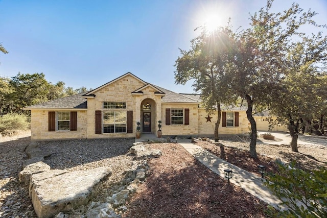 ranch-style house featuring a shingled roof and stone siding