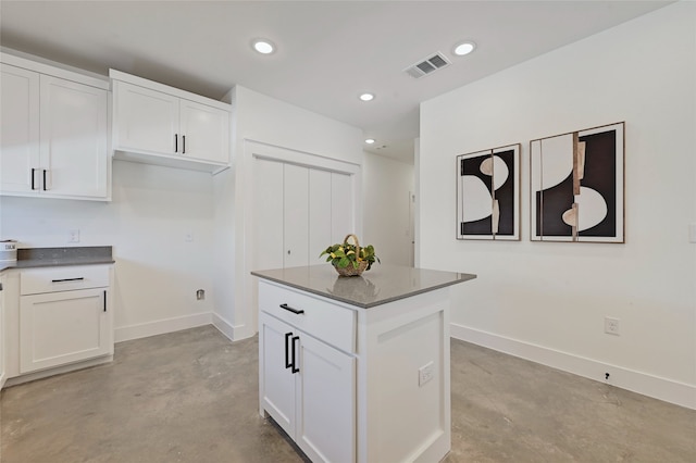 kitchen featuring visible vents, white cabinets, dark countertops, a center island, and concrete flooring