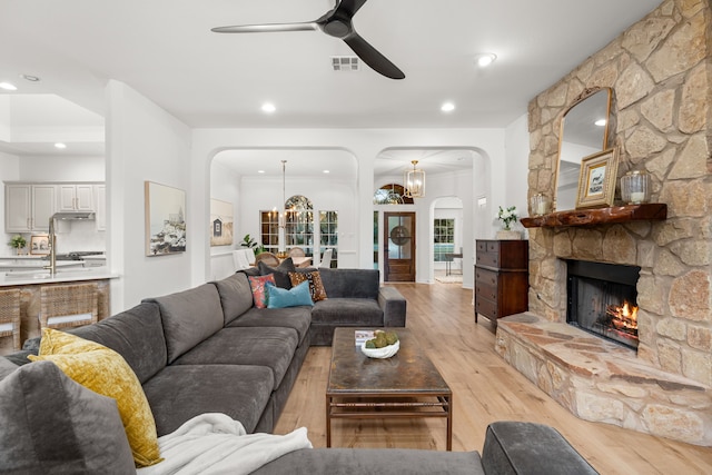 living room with a stone fireplace, light hardwood / wood-style flooring, and ceiling fan with notable chandelier